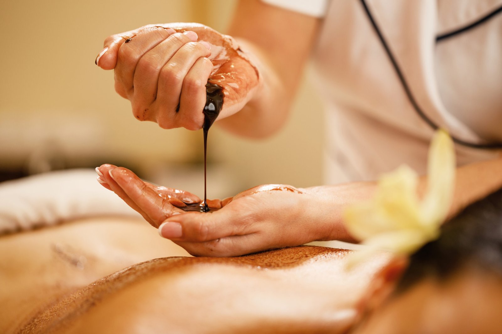 Close-up of massage therapist pouring hot chocolate in her hands before spa treatment. Close-up of therapist preparing for hot chocolate massage at the spa.